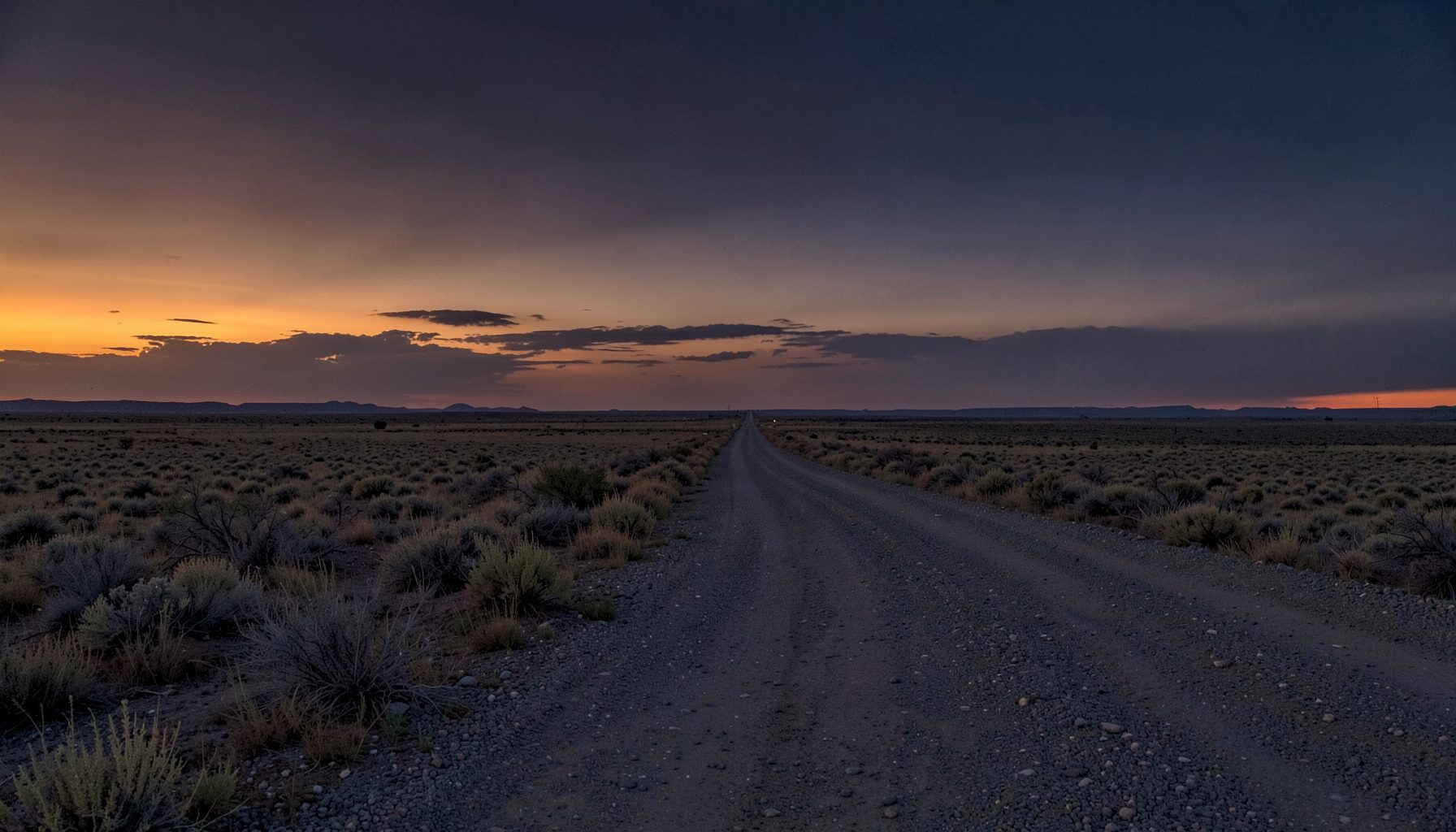 Dusty Colorado high plains at dusk, warm amber and deep indigo sky, wide open landscape with a gravel road stretching into the distance, quiet and atmospheric